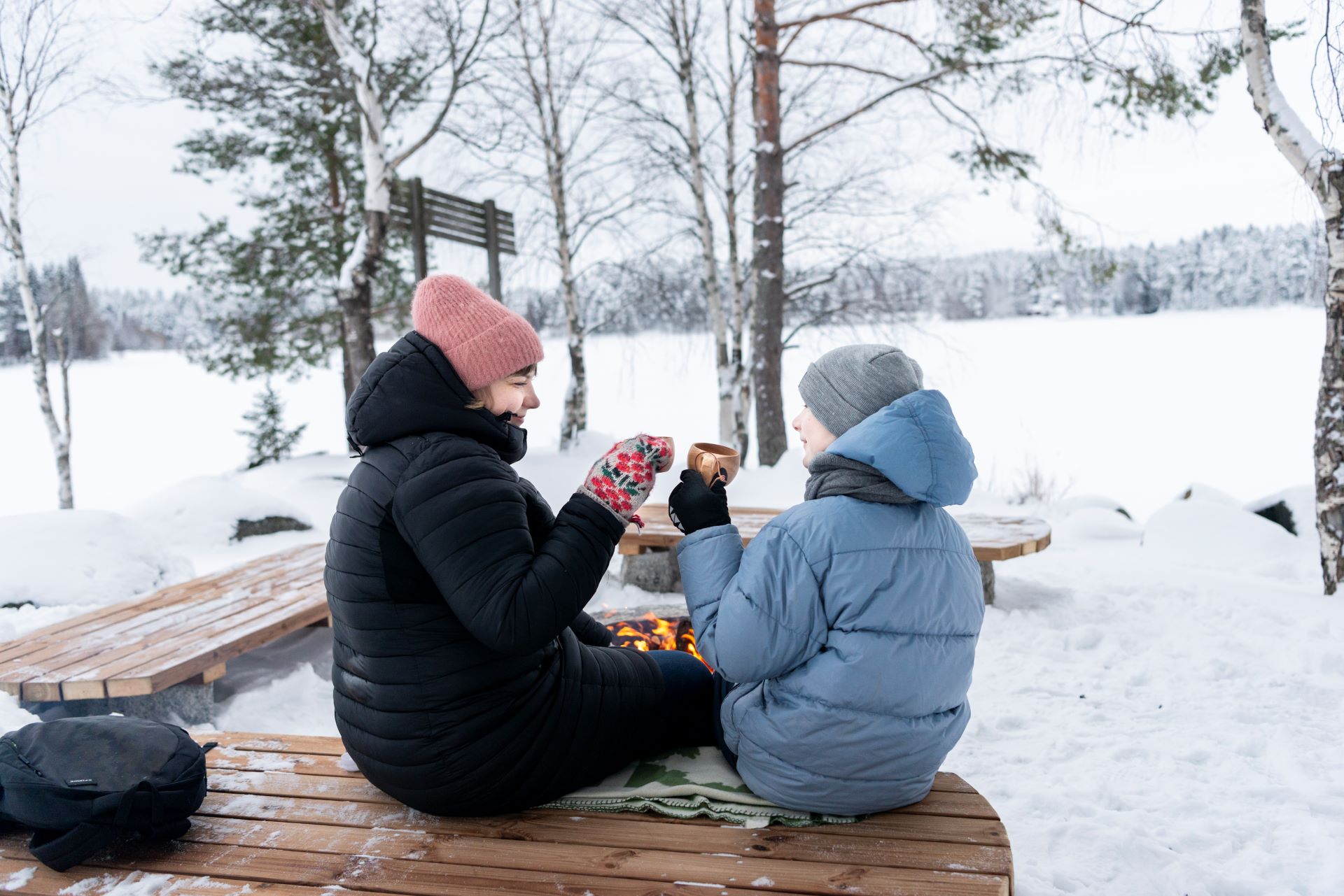 Aikuinen ja lapsi istuvat nuotion äärellä.