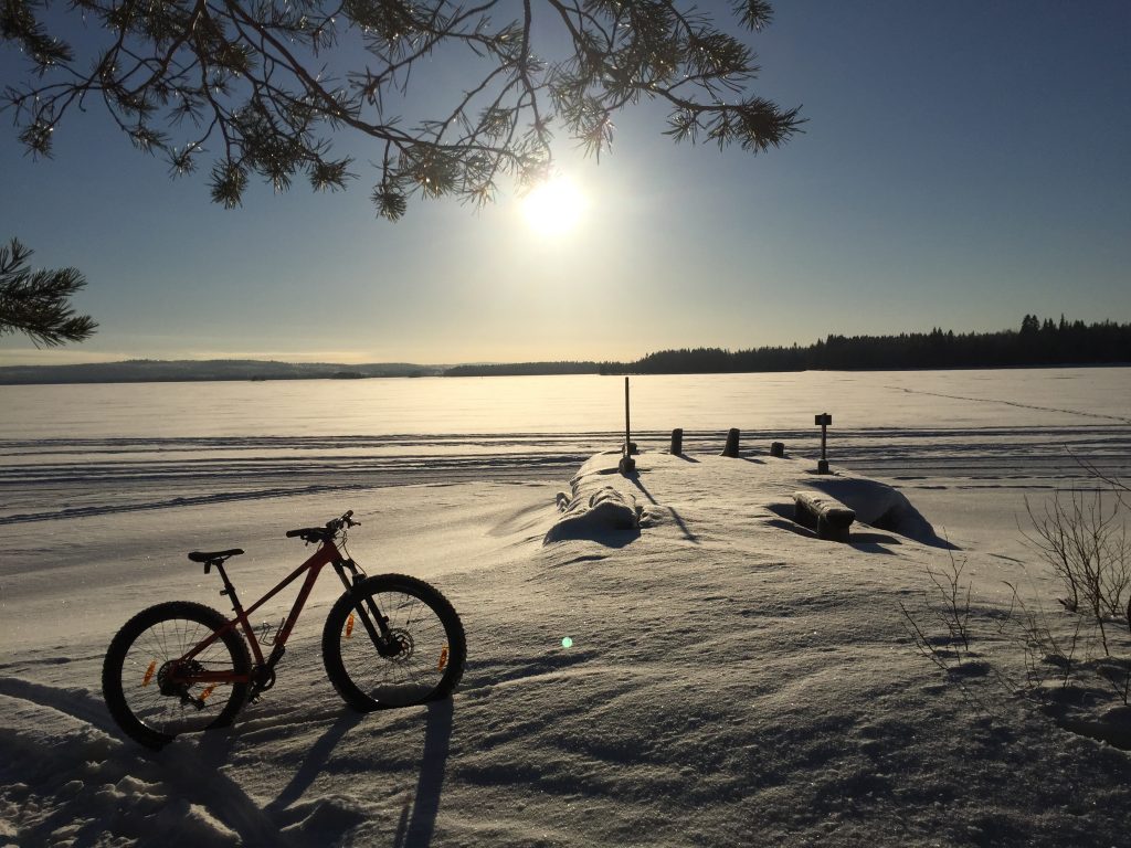 Rehjansaarelta talvella otettu kuva kohti matalalla paistavaa aurinkoa. Maastopyörä on kinoksessa pystyssä.