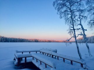 Ruuhijärven laituri talvella. Taustalla aurinko valaisee kaukaisia puiden latvoja.