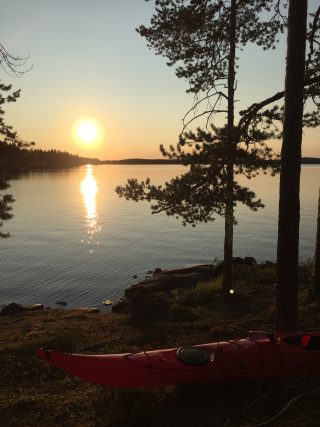 Kuva kanootista Rehjansaaren rannalla. Taustalla auringonlasku.