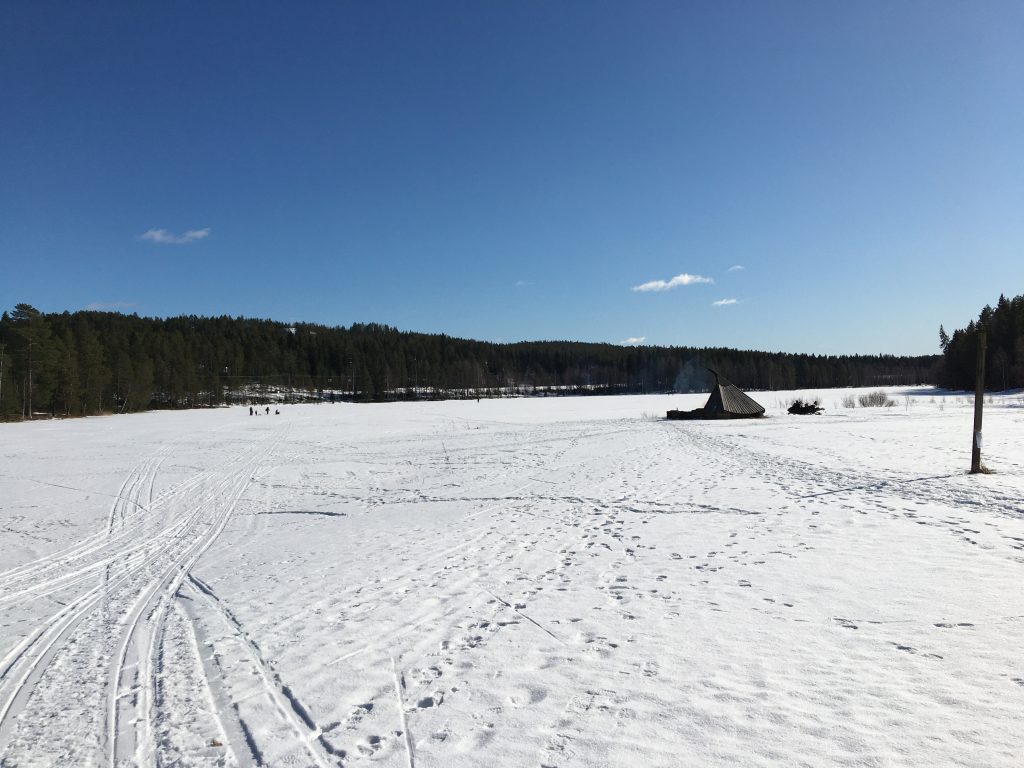 Kuvassa Vimpelinlammen laavu talvella. Lammen jäällä hiihtäjiä.