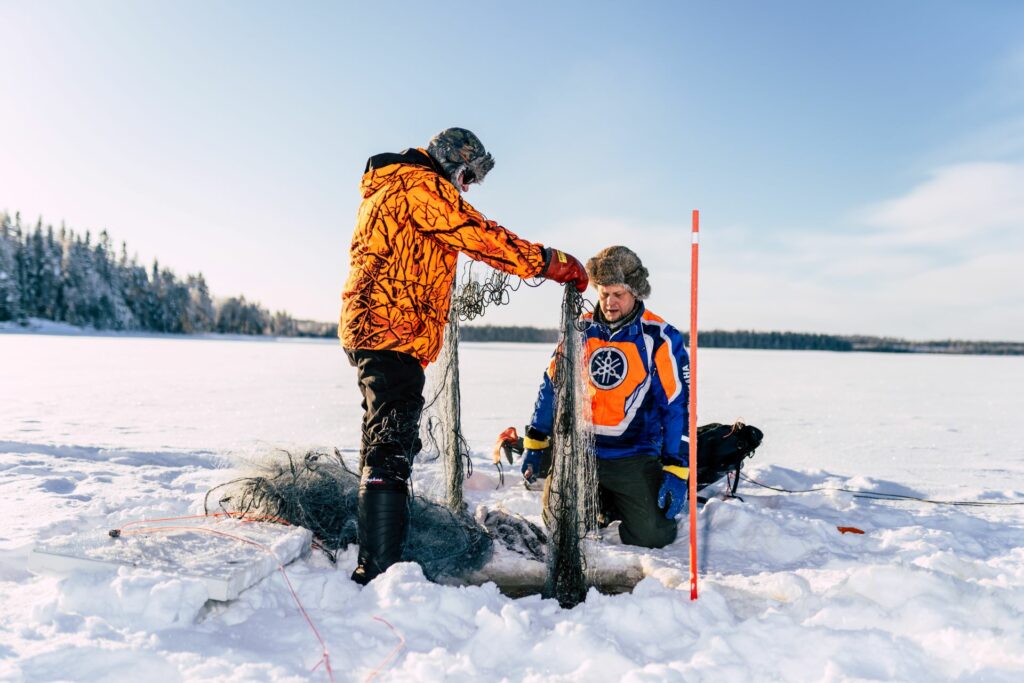 Two men lifting a fishing net from under the ice.