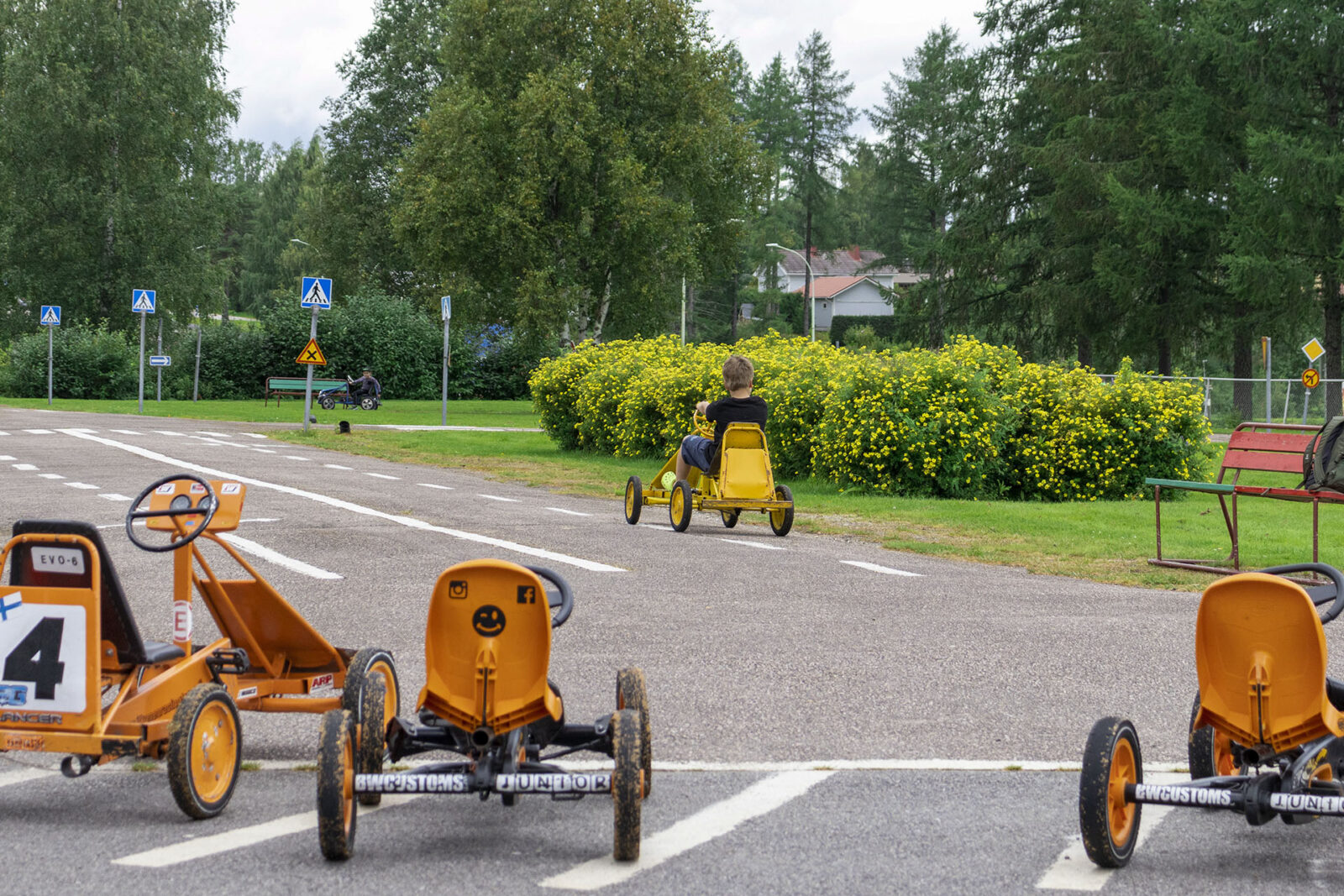 Etualalla polkuautoja parkissa, taustalla kaksi polkuautoilijaa