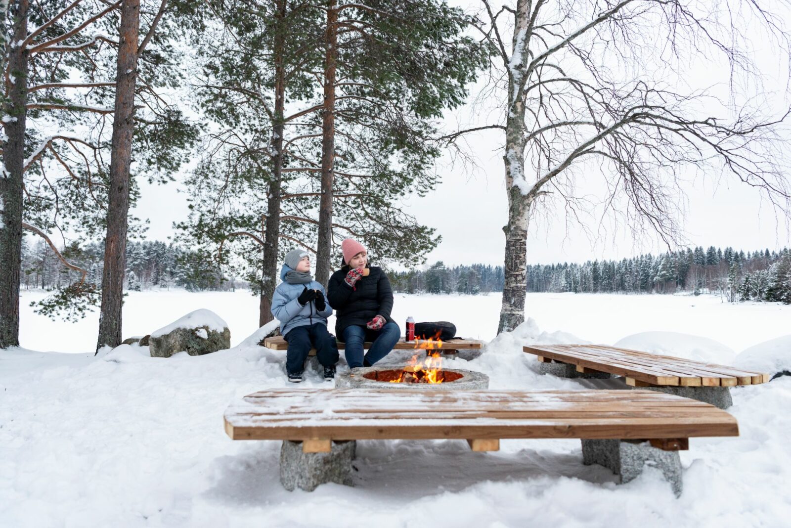 Äiti ja lapsi nauttivat eväitä nuotion äärellä talvella.